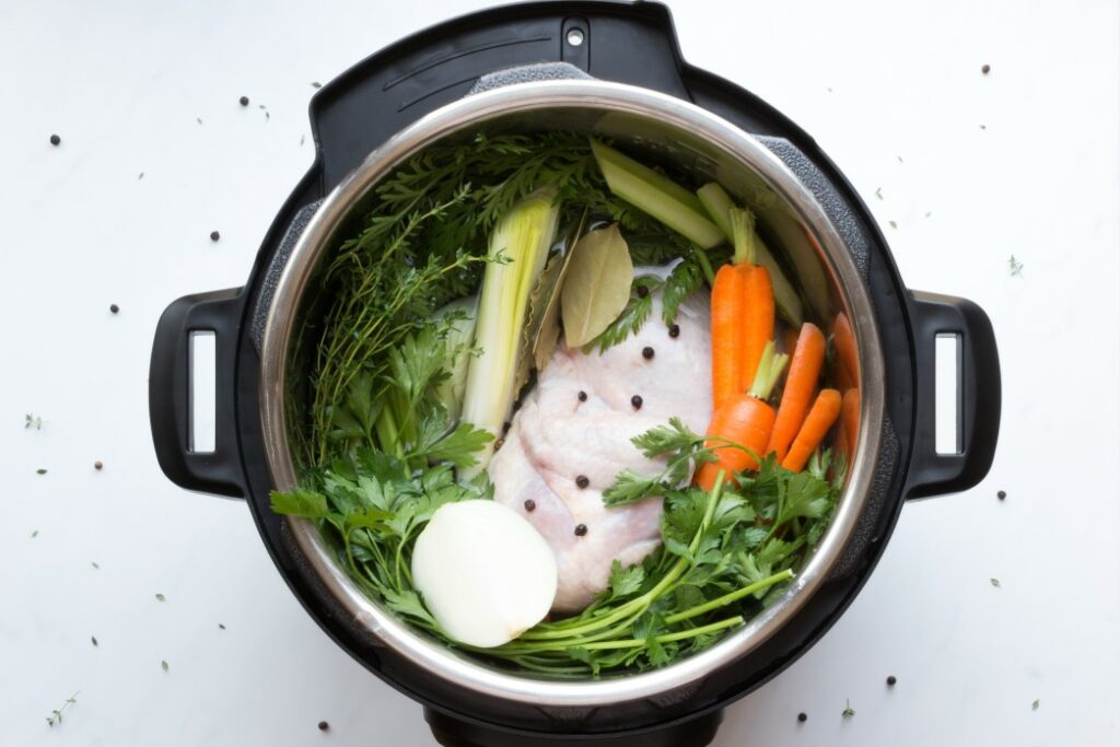 Top down view of vegetables, herbs, and chicken inside of an instant pot ready to be pressure cooked.