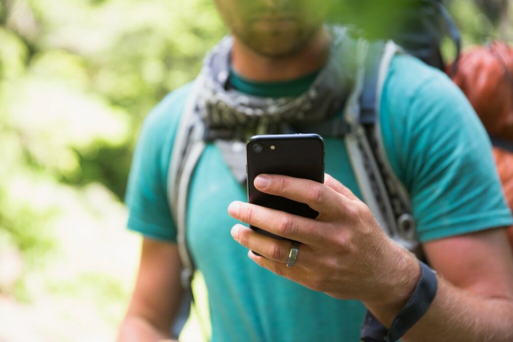 Close up of a black smart phone being used by a man hiking outdoors on a beautiful day.