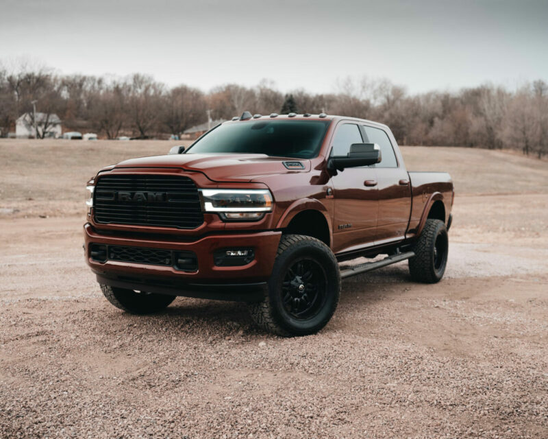 Glamour shot of a 2021 red Ram truck parked in a dirt field with headlights on.