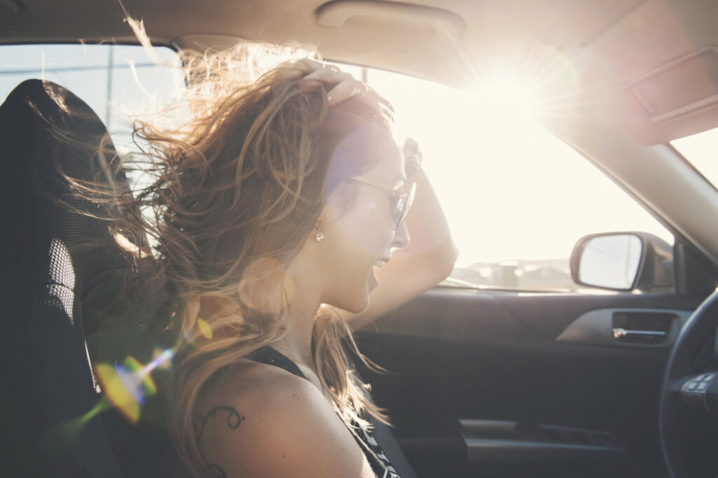 Driver with the windows down, hair blowing in the window, sun streaming through the windows on a road trip.