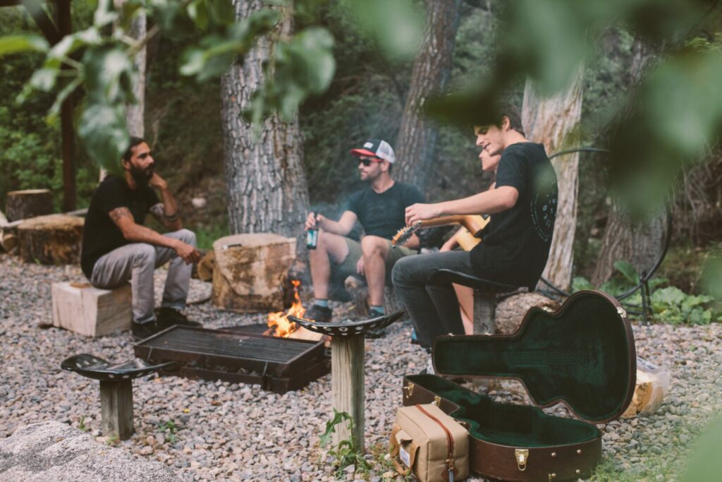 Three men sitting around the campfire drinking cheap beer and playing guitar