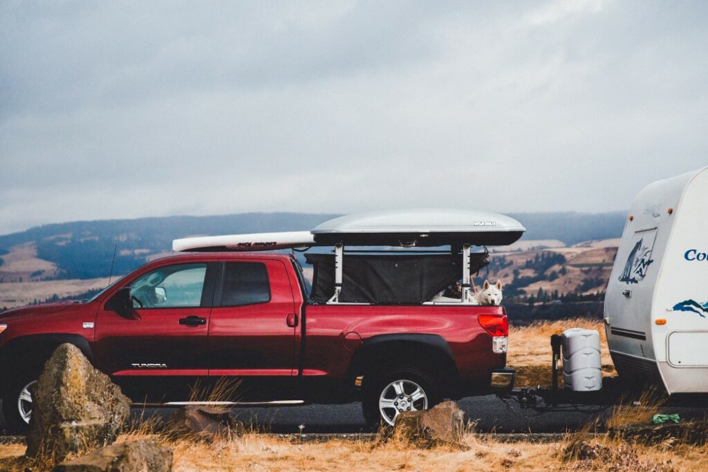Red pick up truck pulls a travel trailer in the wilderness with a white dog in the bed.
