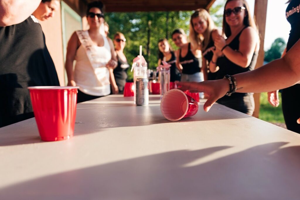 A group of people surround a table playing drinking games with red solo cups.