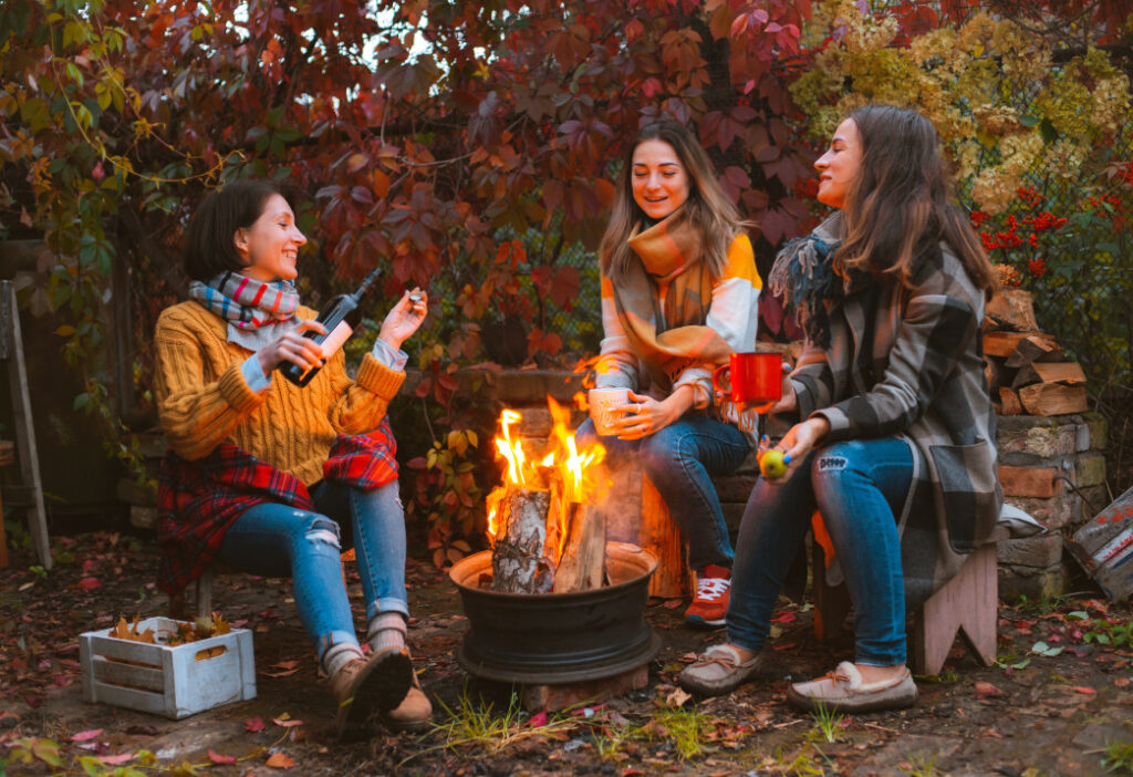 Three women are happy and drinking around a campfire.