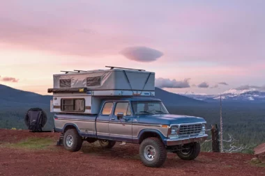 A Four Wheel Camper on a truck set against a sunset and mountains.