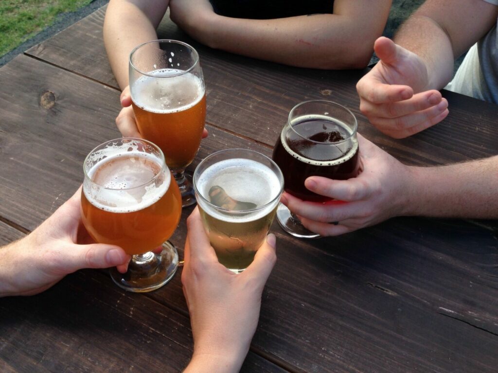 Four friend cheers their beer glasses while sitting at a wooden table