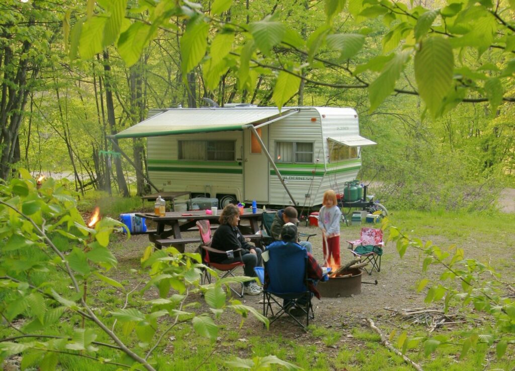 Wooded campsite in Alleghany National Forest, Pennsylvania where a family of four sits around the fire with a picnic table and camper in the background