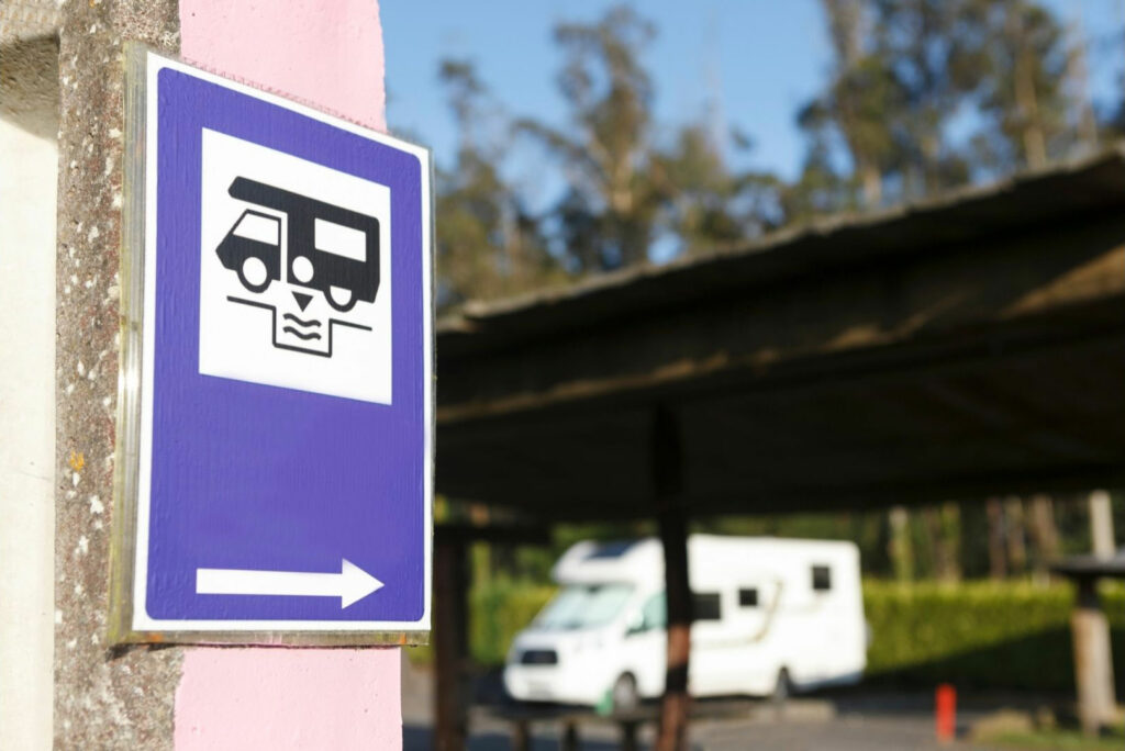 A blue wayfinding sign for a dump station with an RV at the station out of focus in the background.