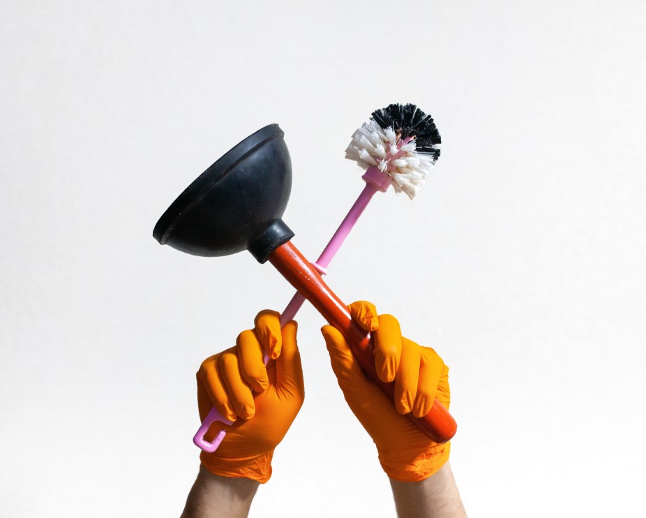 Toilet plunger and scrubbing wand held up by a pair of gloved hands.