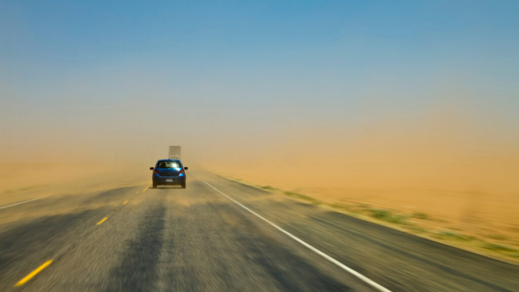 A car drives ahead into a windy dust storm and limited visibility.