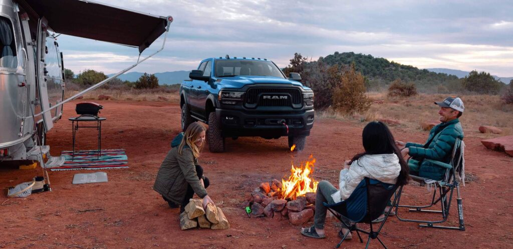 A family sits around a fire outside of their RV in the desert with a Ram 2500 truck parked behind them.
