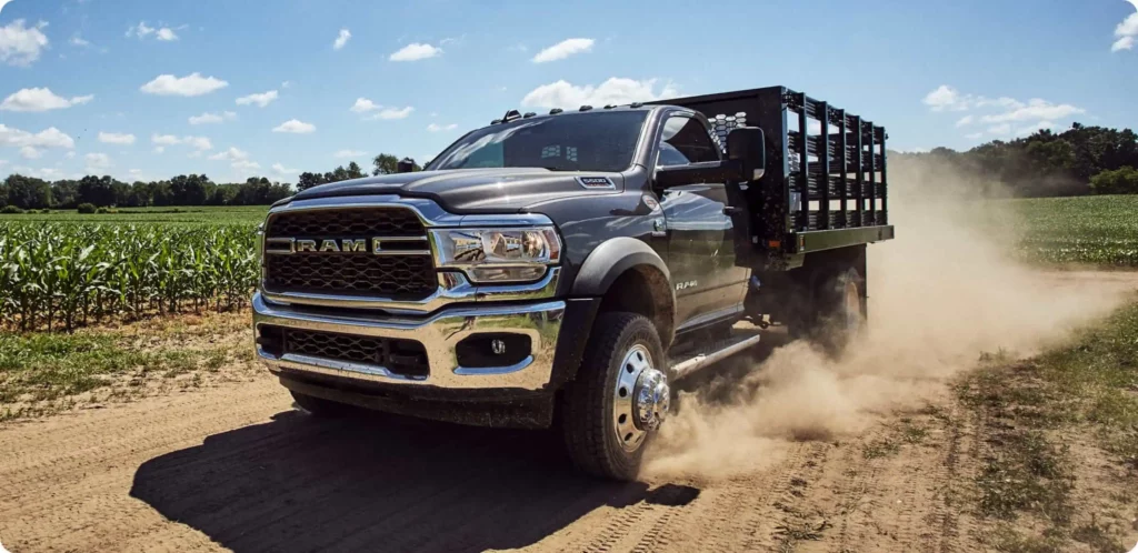 A Ram 3500 Chassis Cab truck is driving quickly through some fields outside and create a plume of dust.