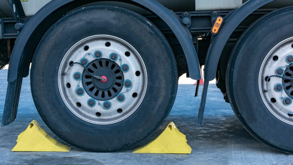 Yellow wheel chocks surround a large vehicle tire.