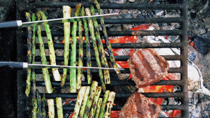 Top-down view of asparagus and steaks cooking on a campfire grill grate