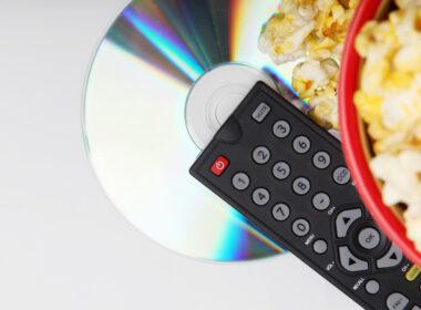 A DVD player remote, a bowl of popcorn, and a shiny DVD.