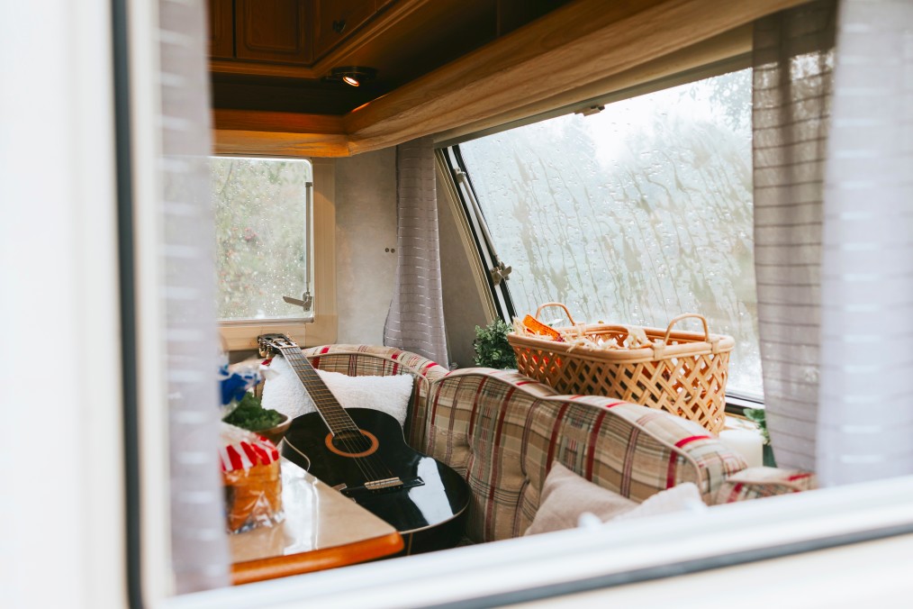 Interior dinette of a small travel trailer with couch cushions, baskets, and a guitar.