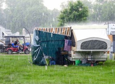 Rain pours down at a campground where a popup caper with an awning and a tarp tries to create shelter.