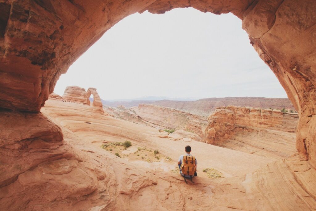A man kneels beneath a giant stone arch in Arches National Park.