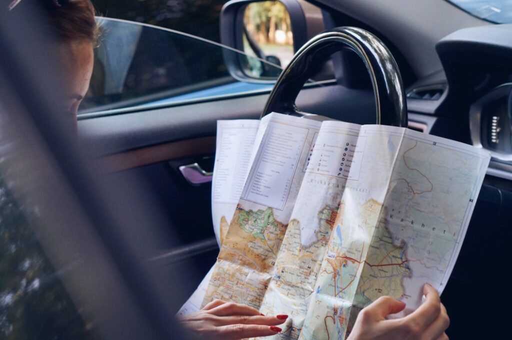 Driver reading a paper map as she lays it against the stearing wheel with the windows down.