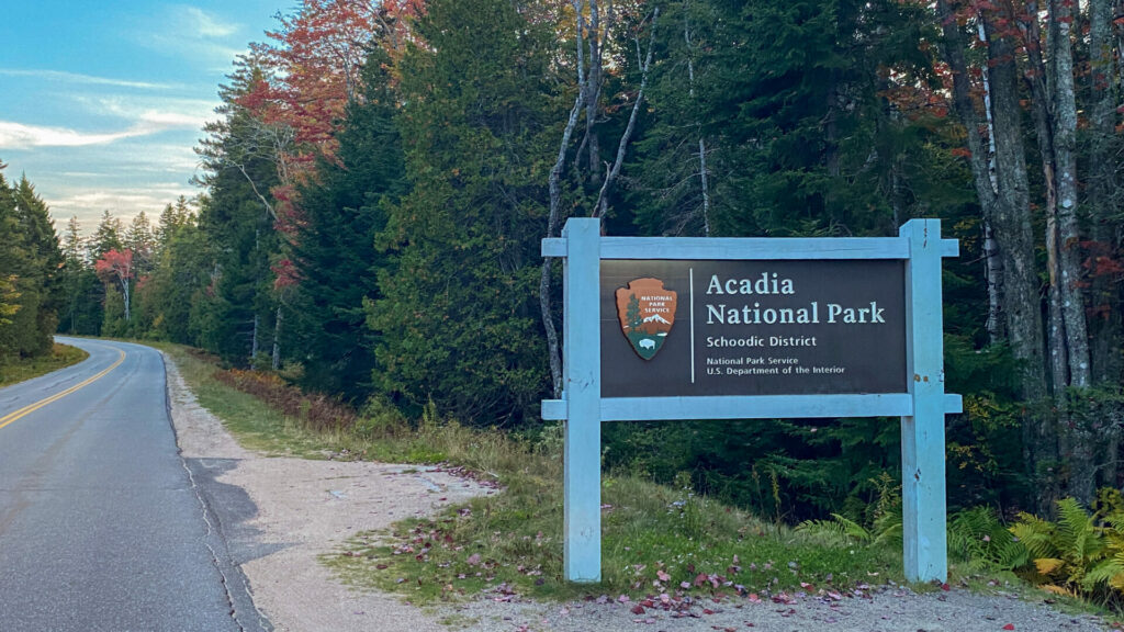 The Acadia National Park sign with colorful trees in the back is a great place to visit in the Fall.