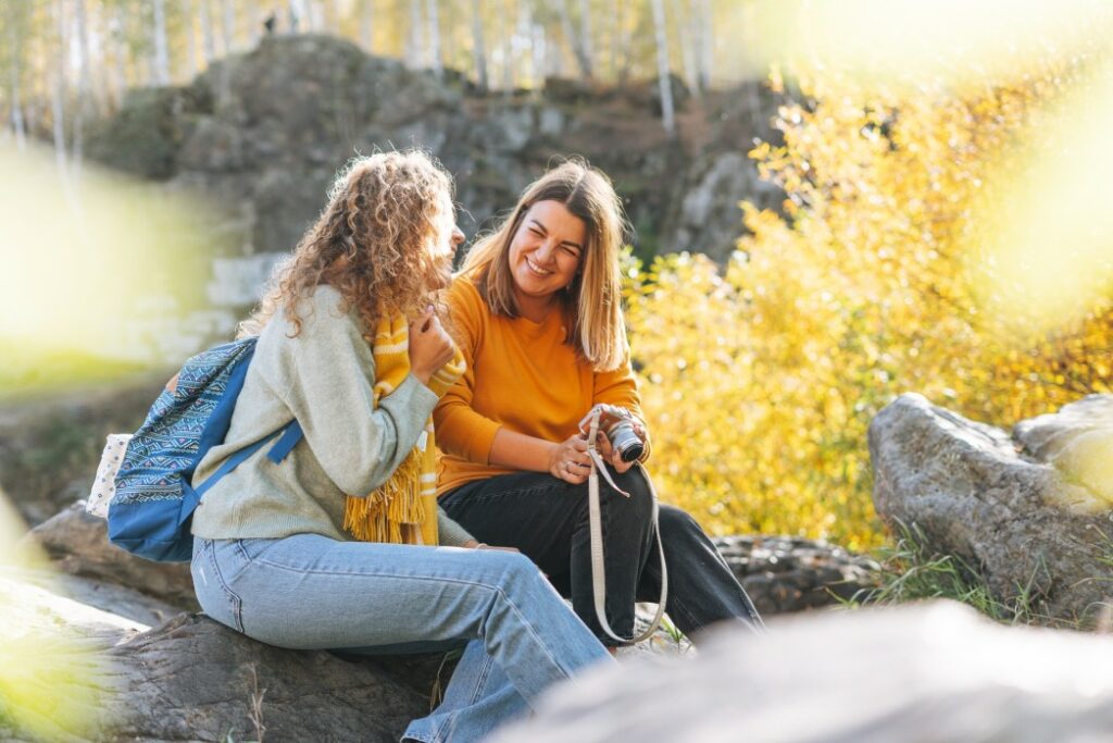 Two women hikers relax and chat while sitting on rocks during their autumnal hike.