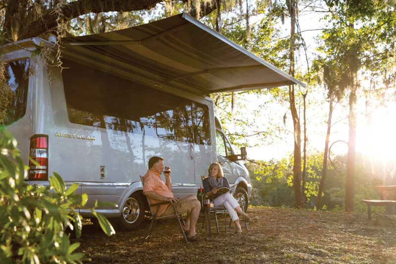 A couple relaxes with win outside of their Airstream Atlas touring coach.