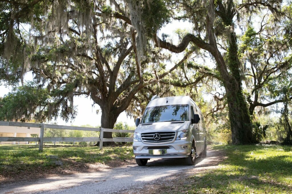 Airstream Atlas traveling down a dirt road with moss hanging down from oak trees lining the road.