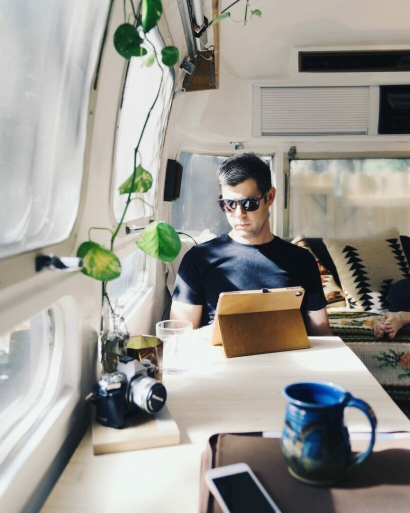 A man uses his digital table at the dinette in his Airstream travel trailer as the sun shines through the windows.
