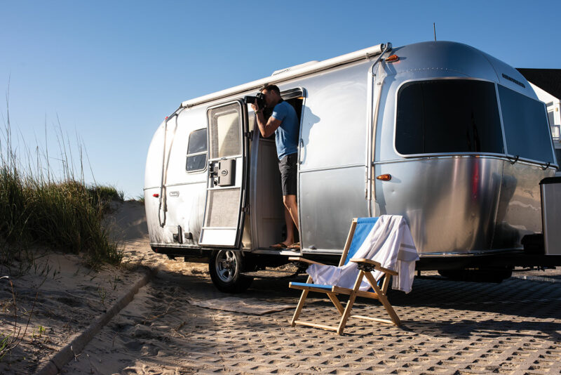A man with a camera shoots out of the front door of his Airstream Bambi travel trailer.