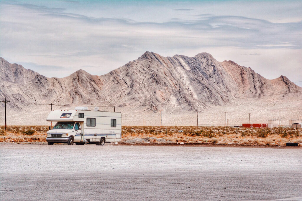 A Class C motorhome parked in a gravel lot with mountains off in the distance.