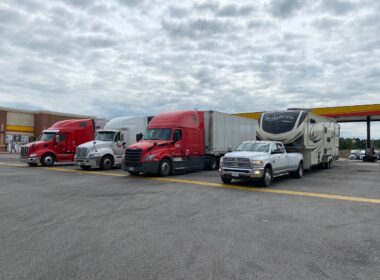 A fifth wheel rv is being towed by a large ram truck and parked next to big rig trucks at a truck stop.