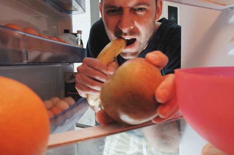 A man grabs fruit from inside his fridge.
