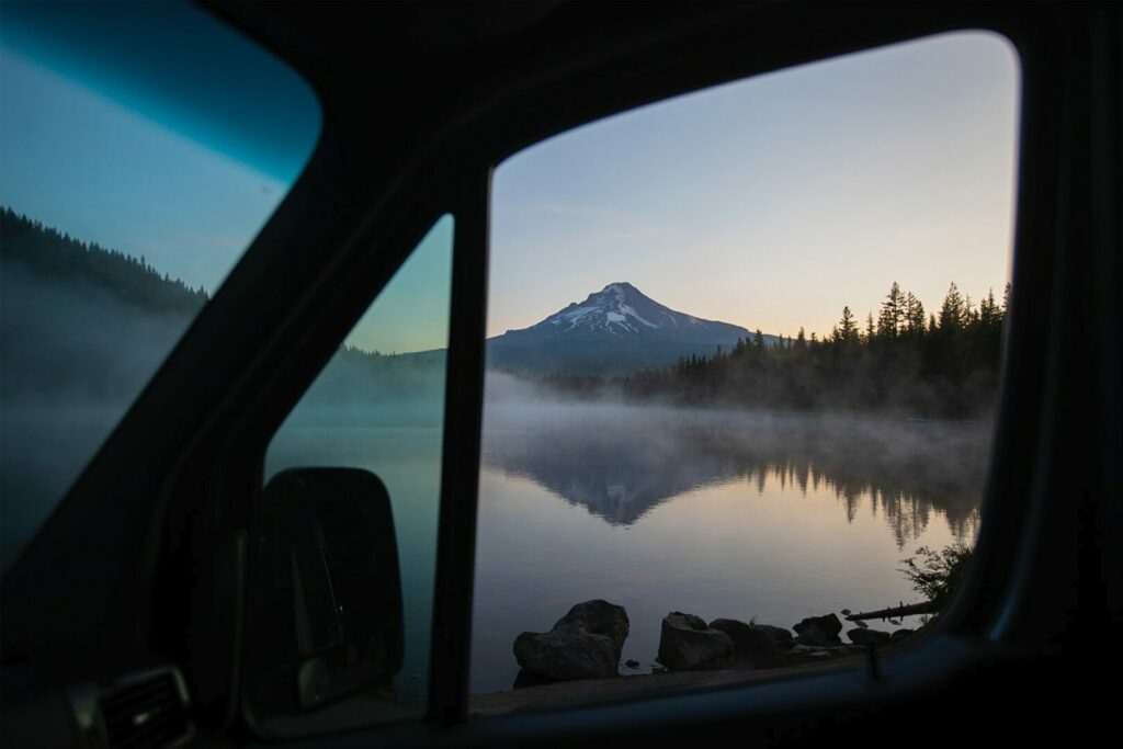 Looking out the passenger window of a motorhome home at the view of a mountain in Seattle reflecting on a steaming lake at sunrise.