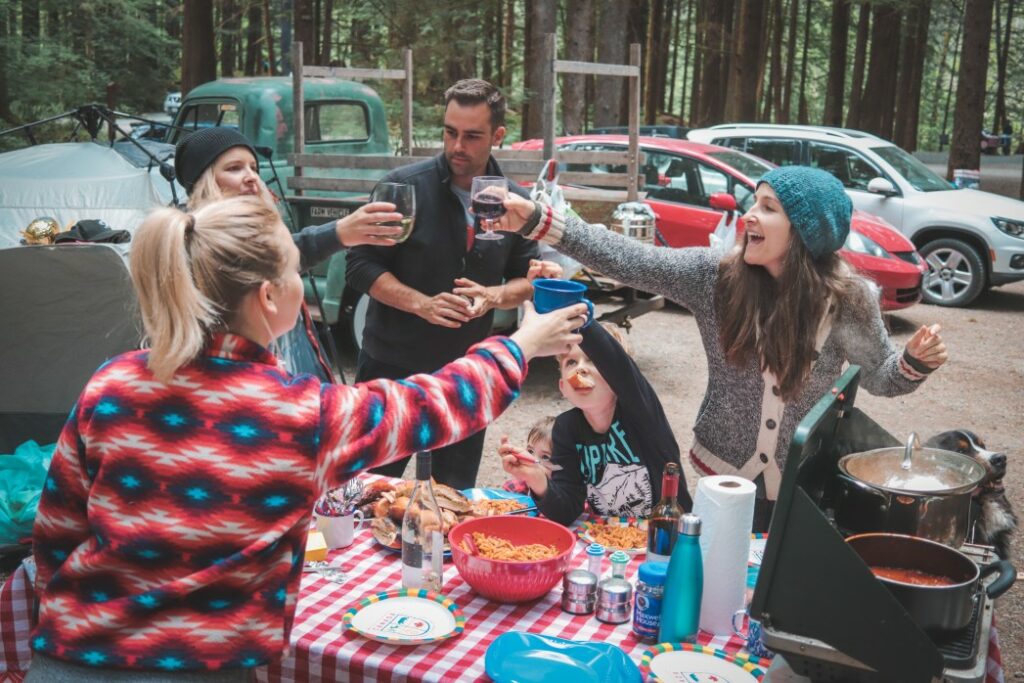 A community of campers enjoy a group dinner at a picnic table and cheers.