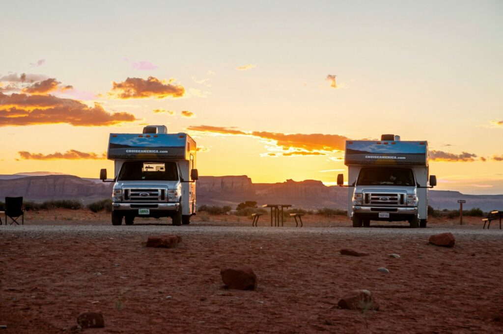 Two rental RVs parked in an RV park in the southwest as the sun sets over red rock formations in the distance.