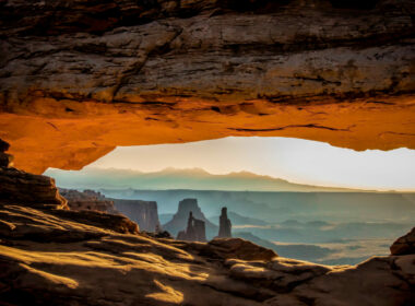Looking through a rock overhang over the desert landscape of Moab as the sun rises.