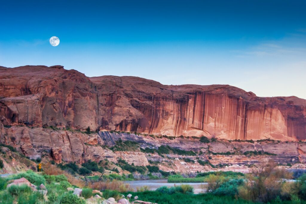 The moon in the early morning sky over the red rocky landscape of Moab.