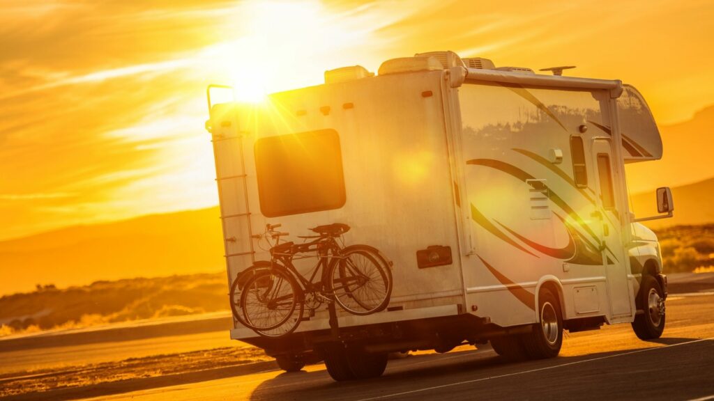 A motorhome drives down a road in the desert on a hot summer day with the sun beating down.