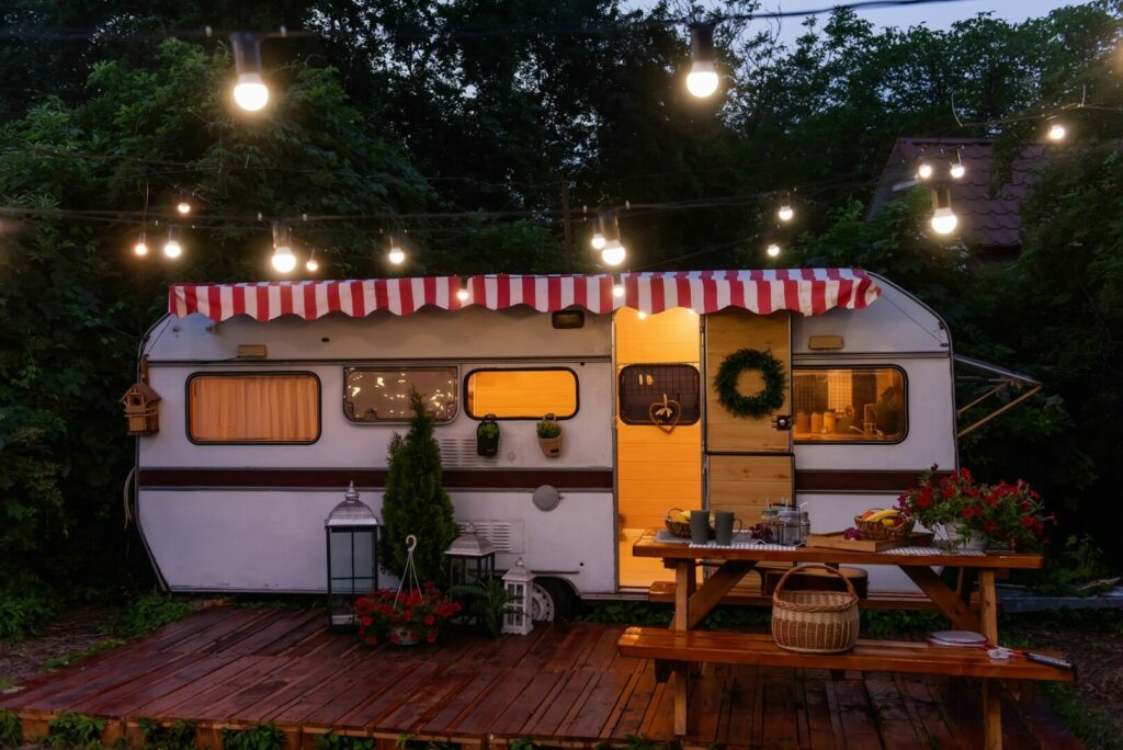 A vintage travel trailer decked out for the holidays with a wreath, Christmas tree, and string lights.