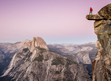 A man stands on a ledge over the epic view of Yosemite Valley which is a national park worth visiting at least once in your life.