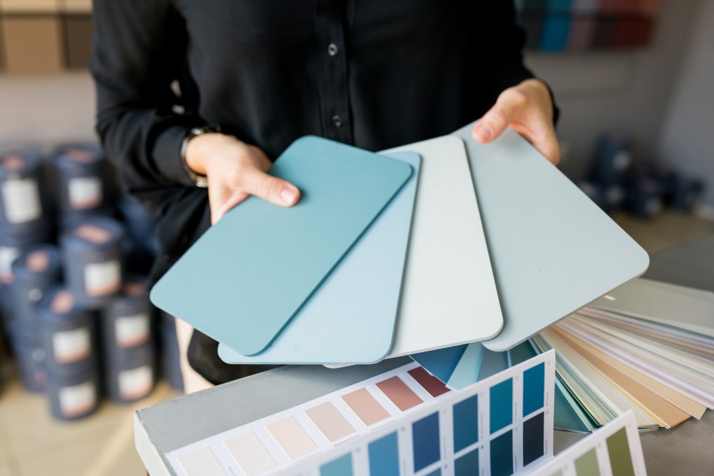 A woman fans out four paint swatches in the blue color familiy.
