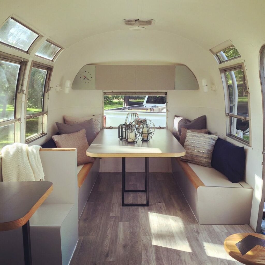 The interior of an Airstream travel trailer with white walls, grey flooring, and a table with benches on either side.