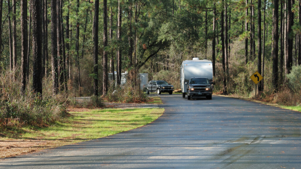 A truck tows a travel trailer around a wide bend in the woods.