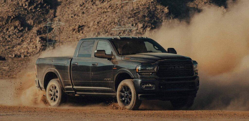 A ram 2500 truck rips up a dirt road and creates a large smoky dust cloud.