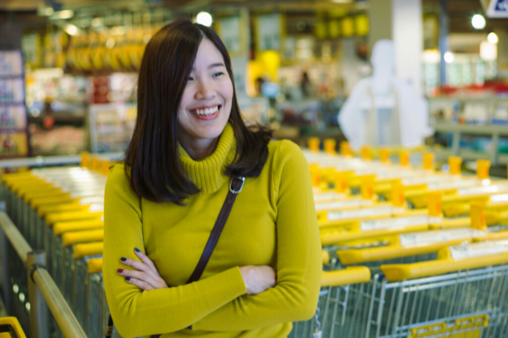 An asian woman smiling in the store in front of shopping carts.