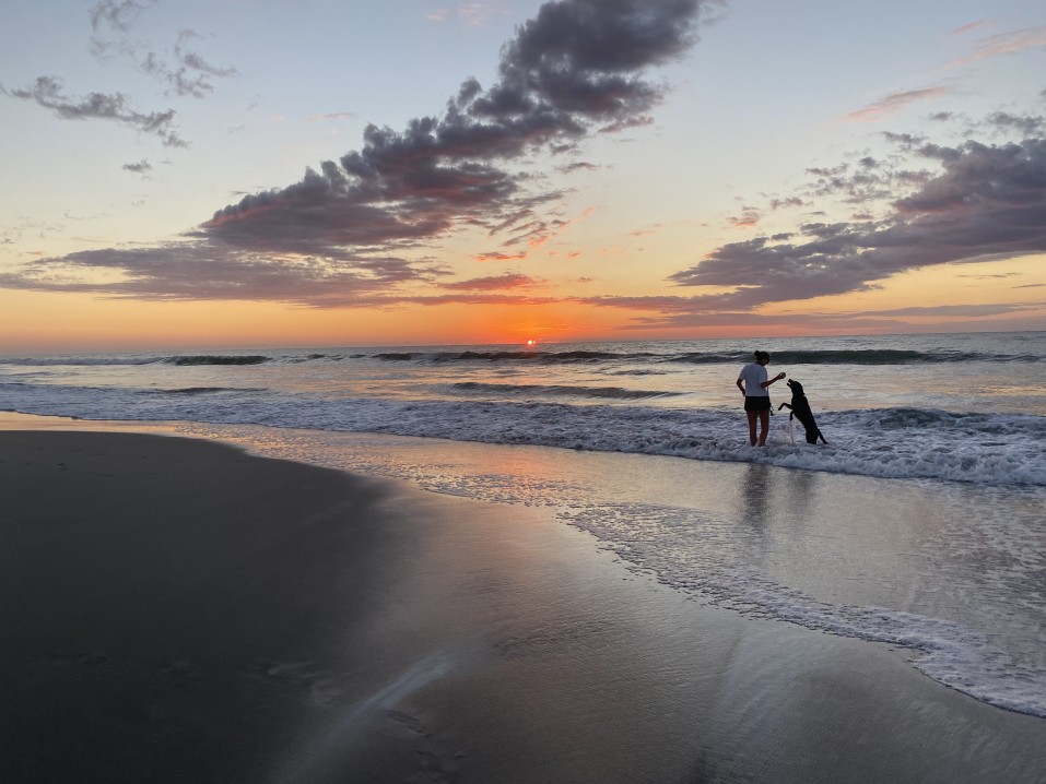 A woman and her dog playing in the waves on Myrtle Beach as the sun goes down.
