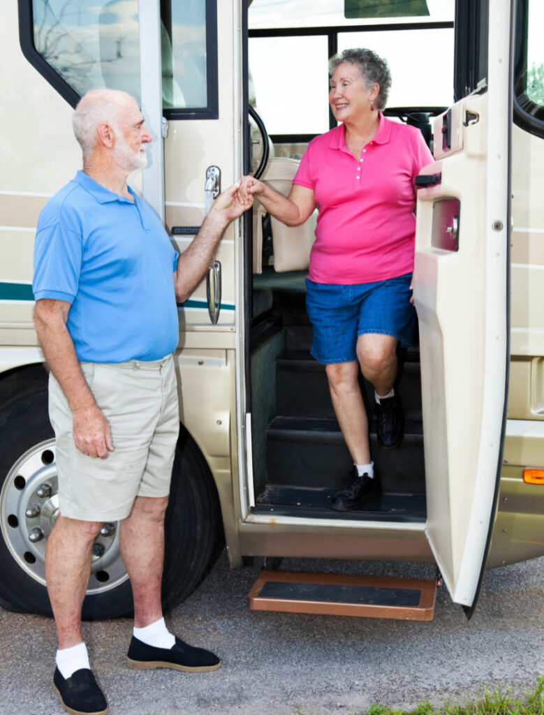 A man helps his wife down the steps to exit their RV.
