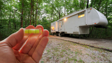 A small bubble held up in front of a fifth wheel parked in a campsite in the woods with it's lights on.
