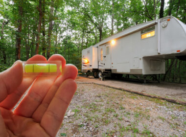 A small bubble held up in front of a fifth wheel parked in a campsite in the woods with it's lights on.