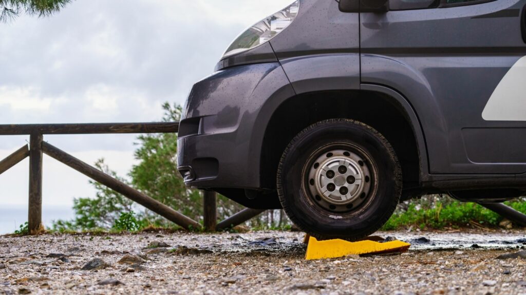 A yellow leveling block underneath the front tires of an RV parked on rocky terrain.